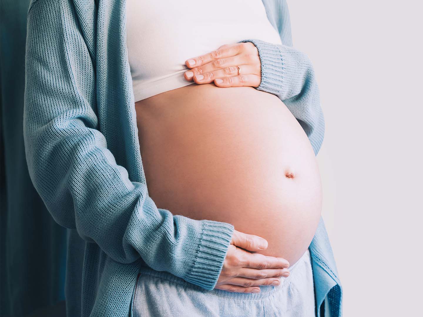 Pregnant woman holds hands on her belly.